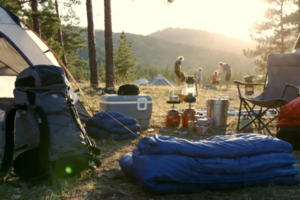 Mountain campsite at sunset with tent, backpack, sleeping bag and camping gear.